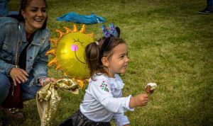Kobieta trzyma zółty balon w kształcie słońca, dziewczynka je loda.