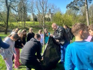 Grupa dzieci wraz z mężczyzna sadzą drzewo w parku