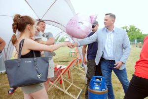 Mężczyzna w niebieskiej marynarce wręcza balon- różowa świnkę dziecki