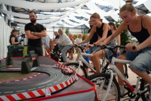 Zdjęcie ukazuje młodzież na rowerkach stacjonarnych, których mocą pedałowania, zasilają tor samochodzikowy